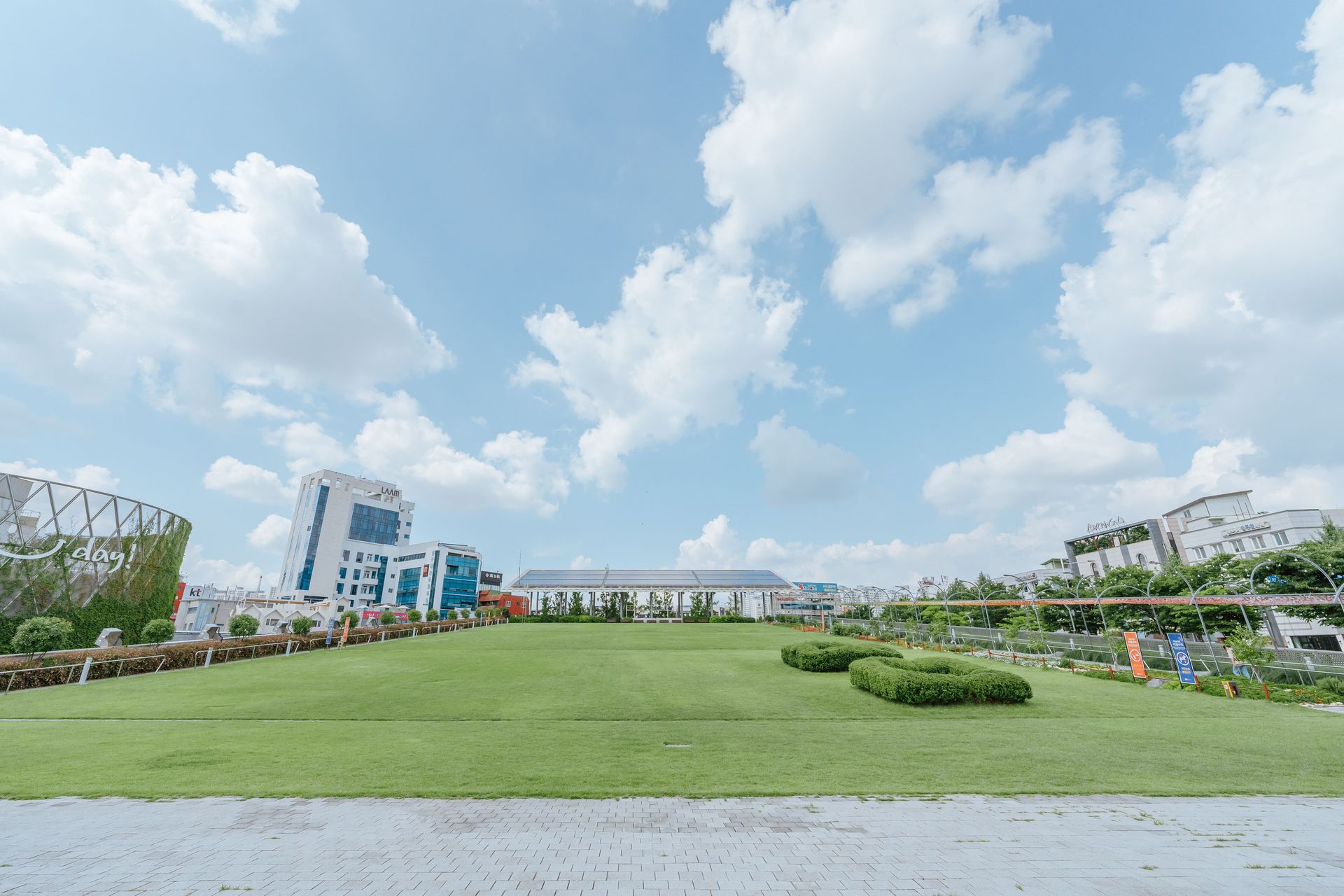 Expansive cityscape featuring modern buildings and a wide grassy area under a bright blue sky.